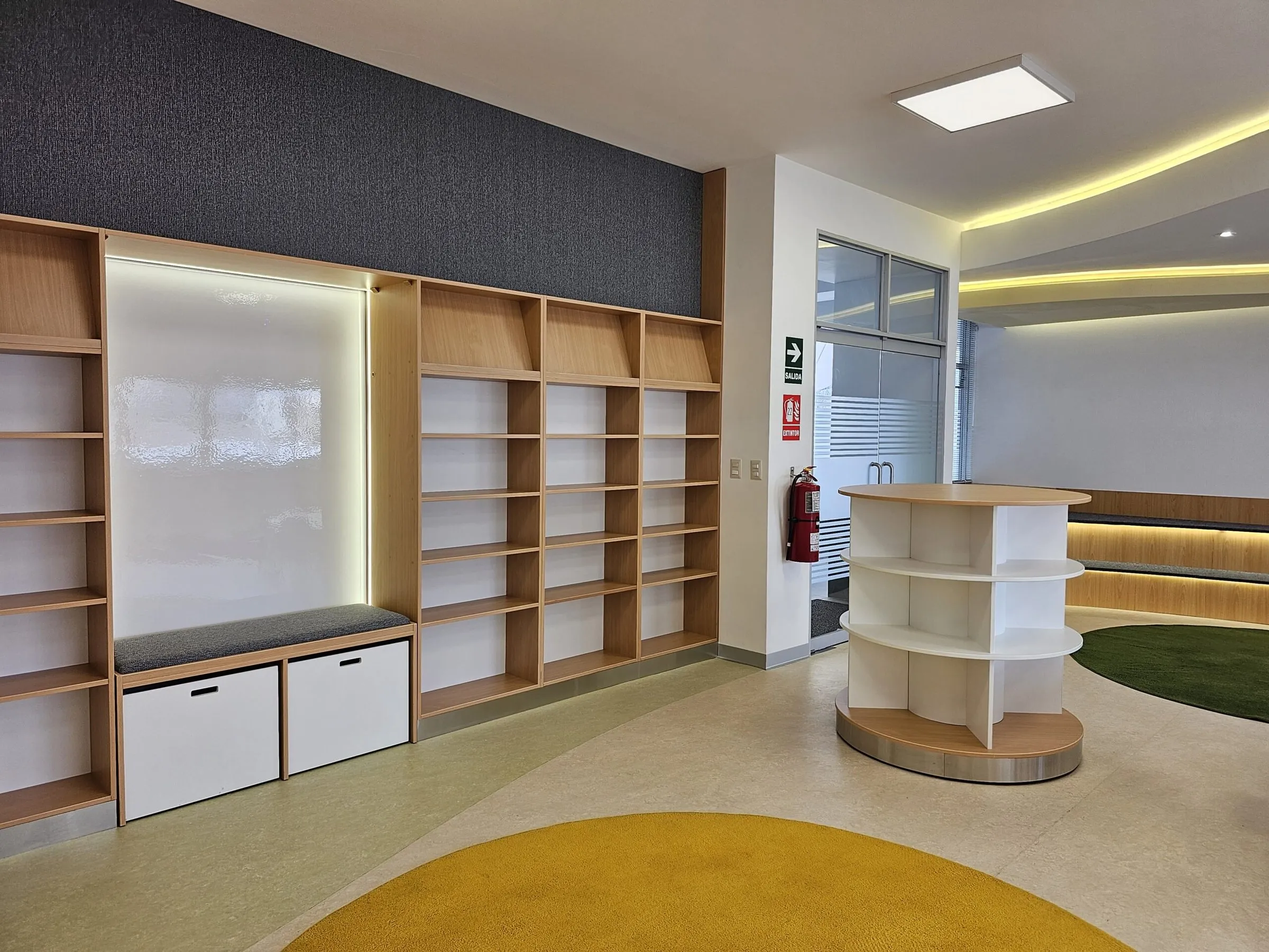Estantería de madera con pizarra, el mueble circular y la alfombra amarilla.