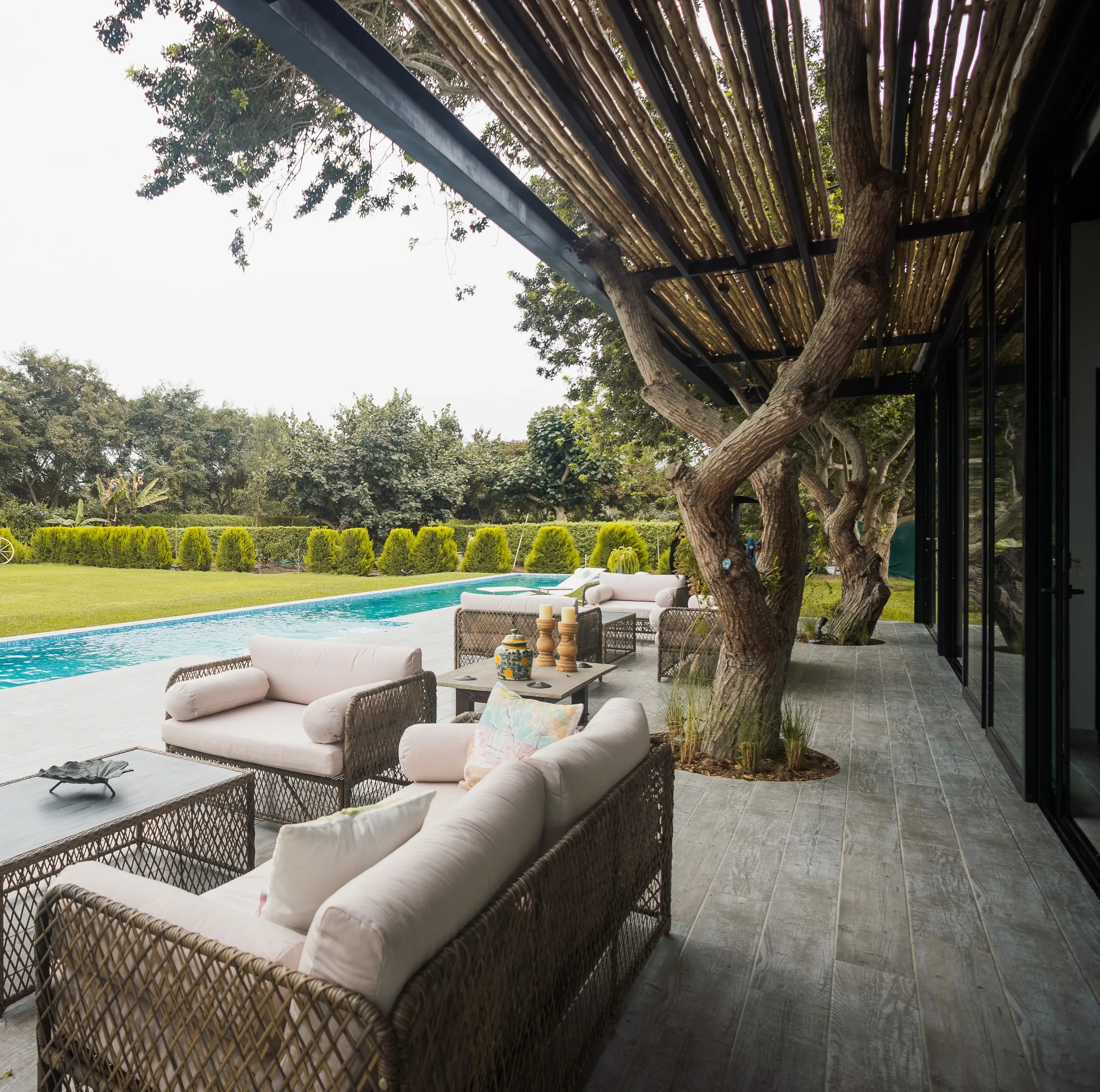 Terraza de Casa Larrabure con pérgola de madera, un árbol que atraviesa el techo, sala exterior y piscina.